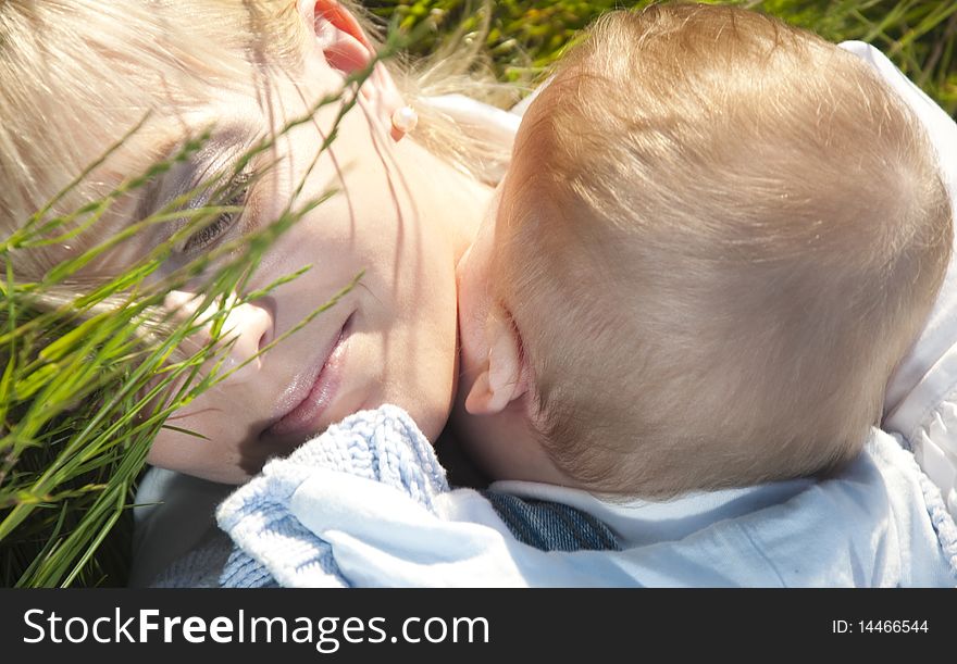 Young happy mother with a child lying embraced on the green grass in the park