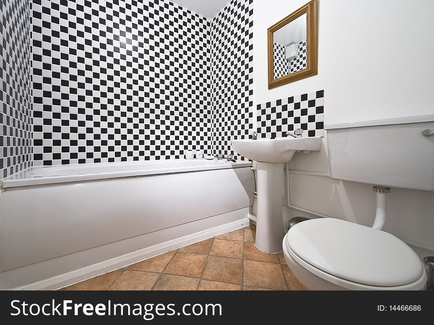 Classy bathroom with large bath tub, white ceramic wash basin and toilet with black and white chessboard pattern tiles. Classy bathroom with large bath tub, white ceramic wash basin and toilet with black and white chessboard pattern tiles