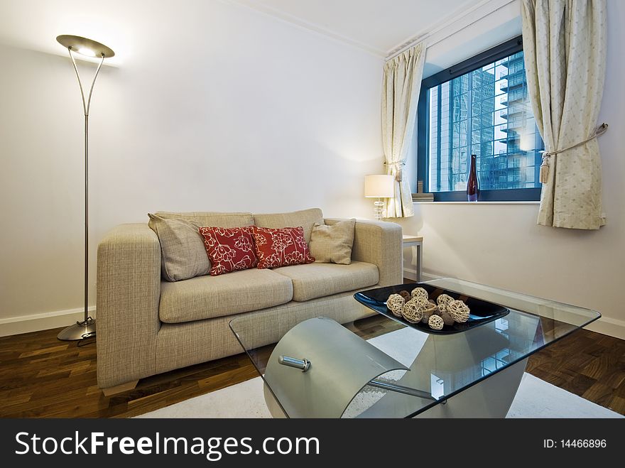 Modern living room with beige sofa with decorative cushions and glass top designer coffee table