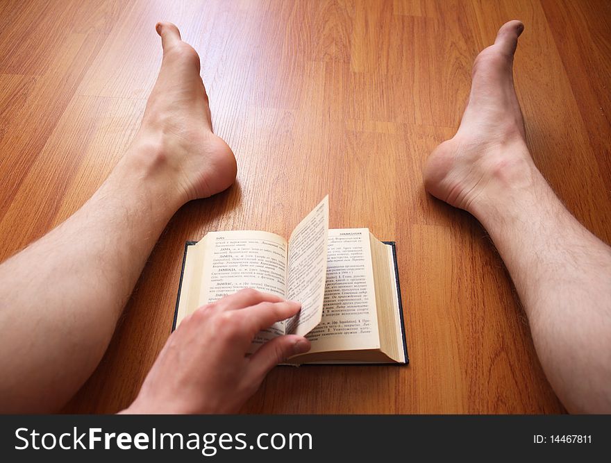 The person sits on a floor and reads the book. The person sits on a floor and reads the book