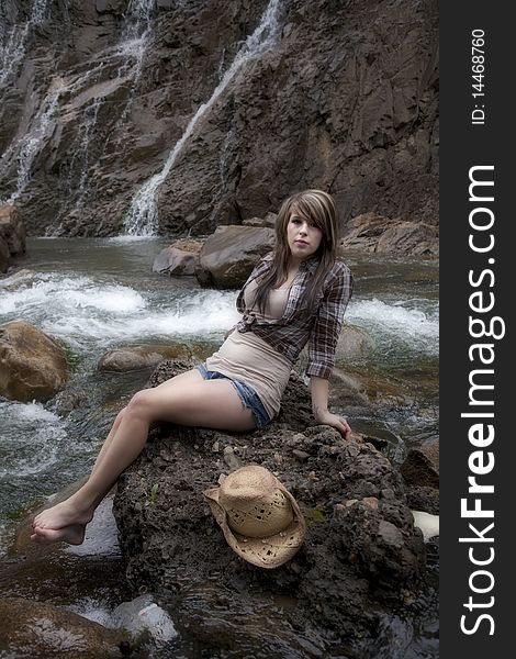 A beautiful woman dressed like a cowgirl on a rock by the river. A beautiful woman dressed like a cowgirl on a rock by the river.