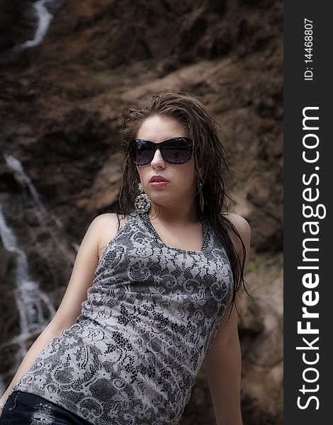 A woman in a great tank top and sunglasses in front of a waterfall. A woman in a great tank top and sunglasses in front of a waterfall.