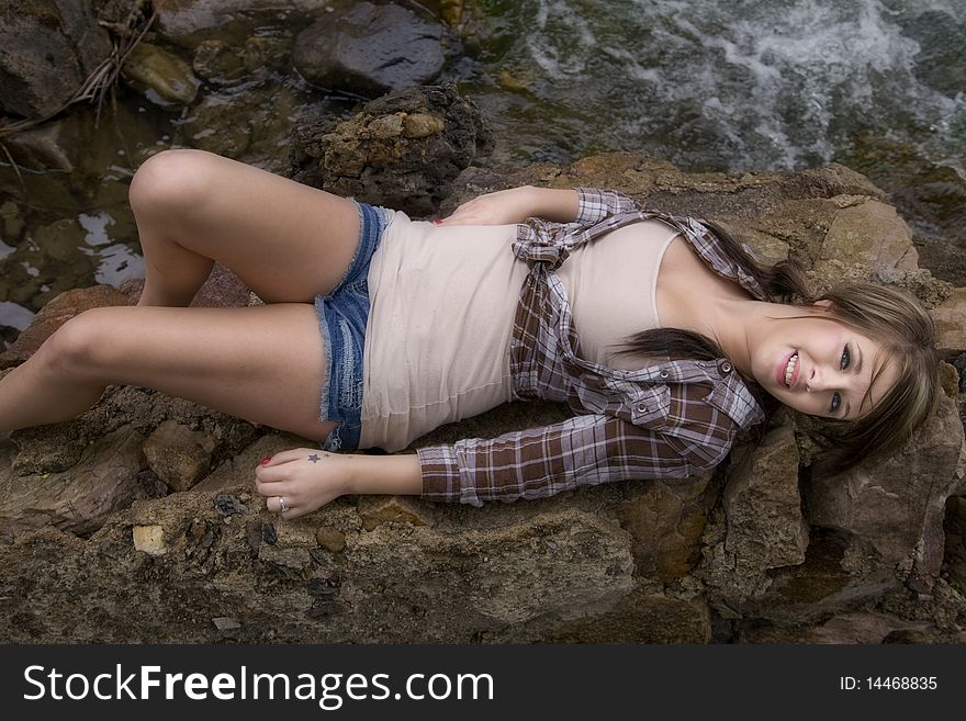 A woman is laying on her back on a big rock with the river right by her. A woman is laying on her back on a big rock with the river right by her.