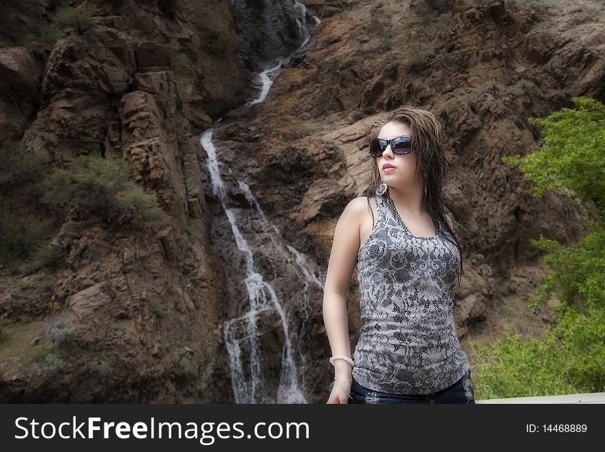 A woman is looking to the side by a waterfall and with sunglasses on. A woman is looking to the side by a waterfall and with sunglasses on.