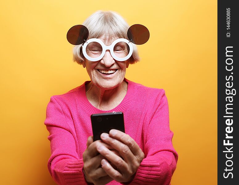 Old grandmother is talking to her grandchildren by phone, smiling and greeting them.