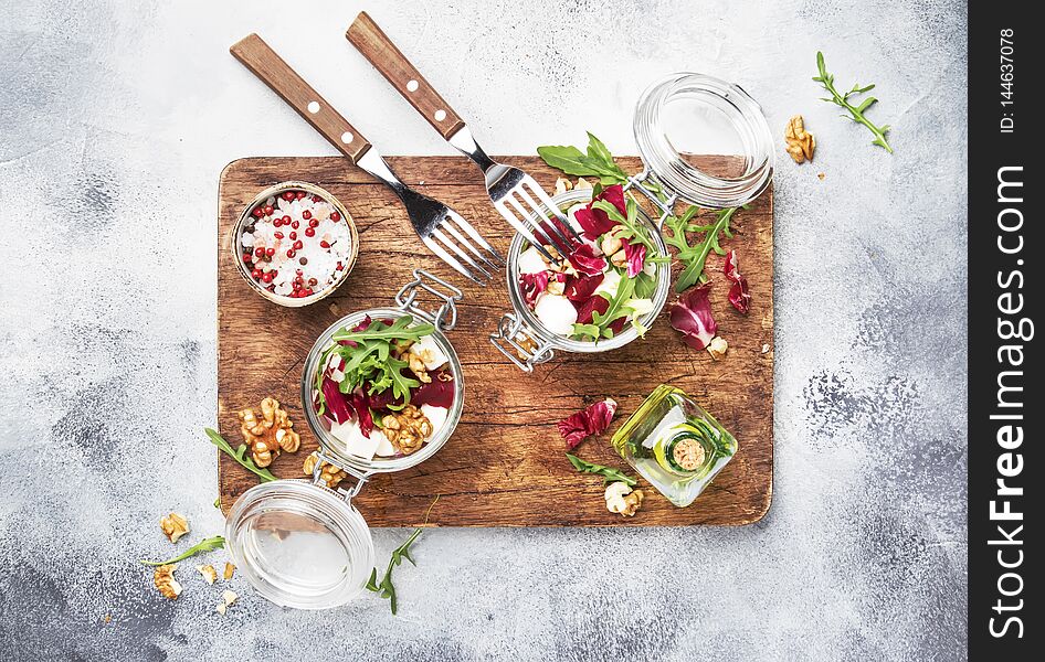 Beet or beetroot salad with fresh arugula, soft cheese and walnuts, trendy salad jar, piece on a fork, gray kitchen table