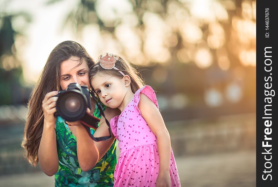 Mother and daughter taking photos with camera at sunset