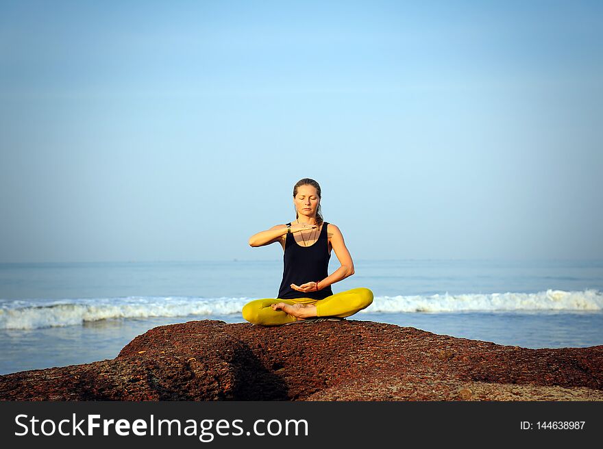 Beautiful young woman practicing yoga and stretching exercises at the summer ocean beach