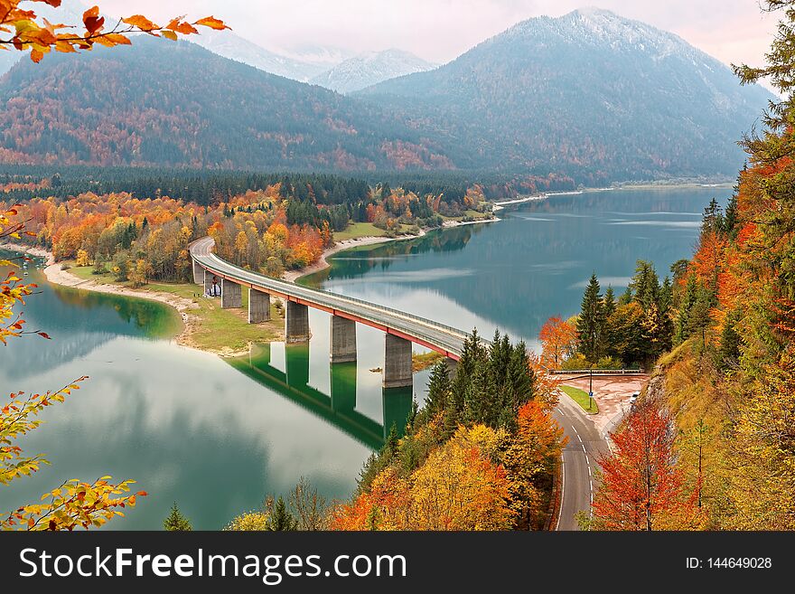 Scenic view of a curved bridge over Lake Sylvenstein with beautiful reflections on smooth water, colorful foliage by lakeside