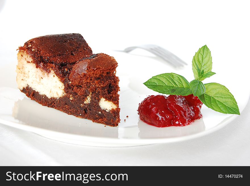 Cheese-brownie with raspberries jam on a white plate, served with mint leaves