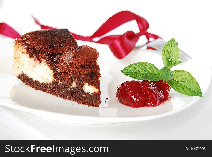 Cheese-brownie with raspberries jam on a white plate, served with mint leaves.