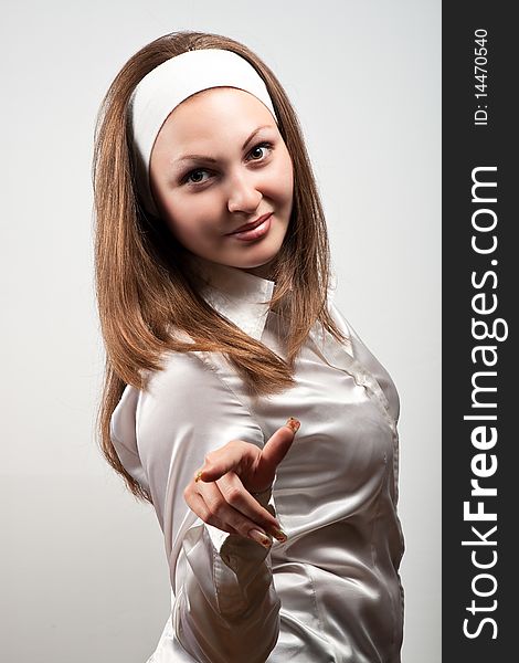 Young smiling woman dressed white illustrates somthing with finger over gray background. Young smiling woman dressed white illustrates somthing with finger over gray background