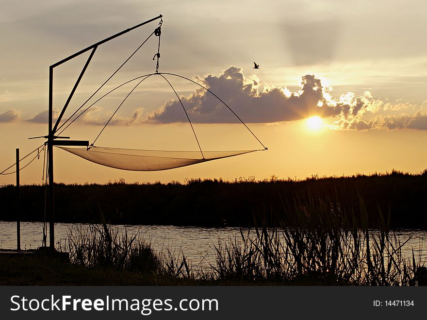 A fishing net suspended over a river at the sunset