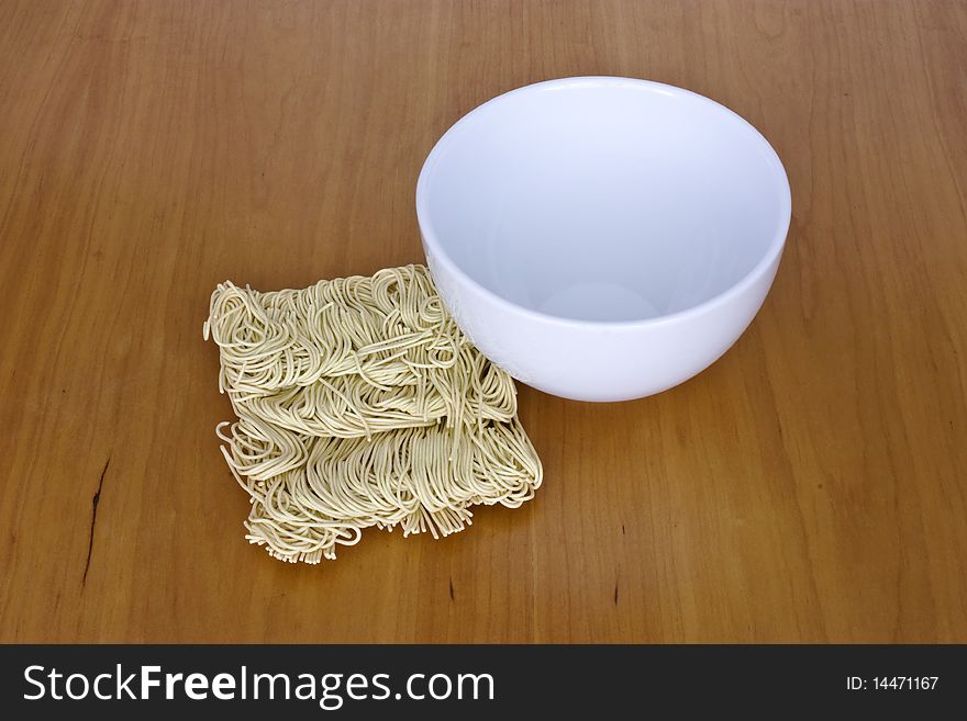 A simple white bowl beside dried noodles on a wooden table. A simple white bowl beside dried noodles on a wooden table