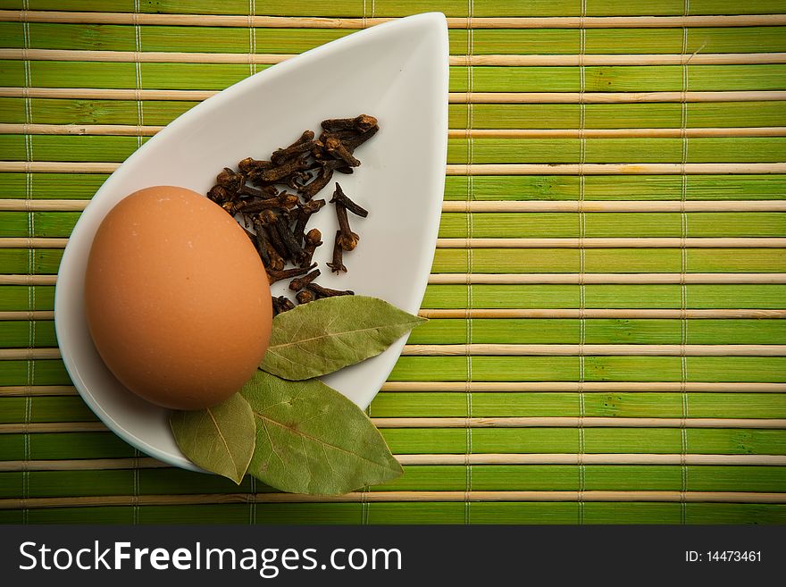 Egg and laurel leaves in a white container in the green bamboo mat