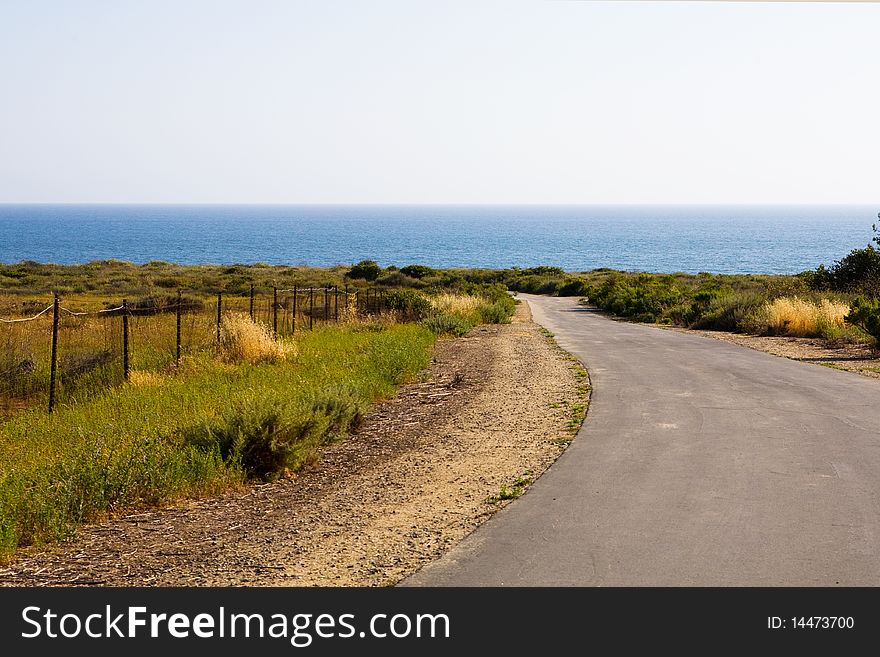 A one-lane country road leads through a field down toward the beach. A one-lane country road leads through a field down toward the beach.