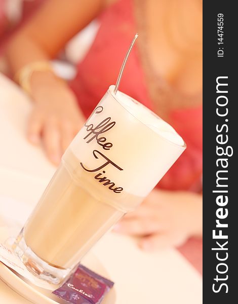 A glass with lettering coffee time a spoon and a cookie on a table