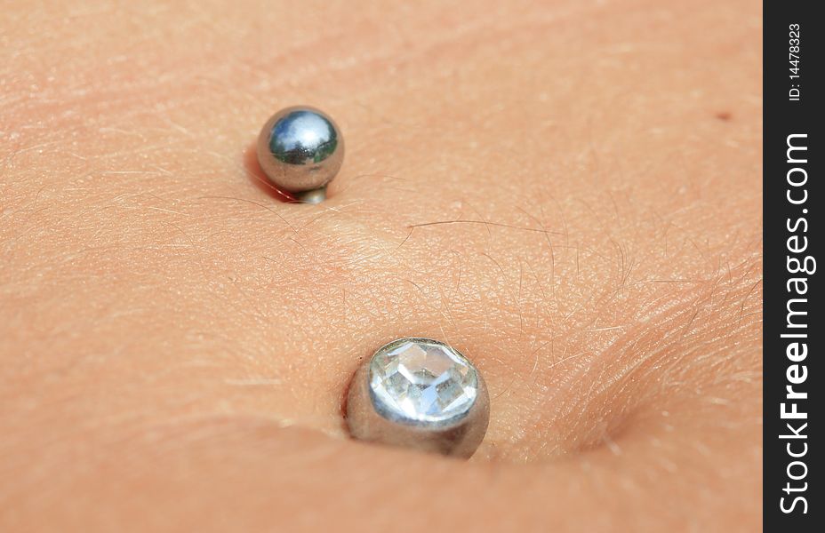 Small ear ring with a pebble in a navel of the girl