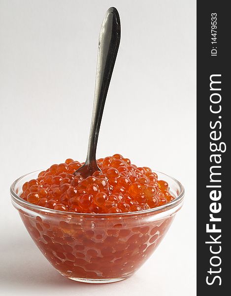 Red caviar in the little glass bow and spoon isolated over grey gradient background