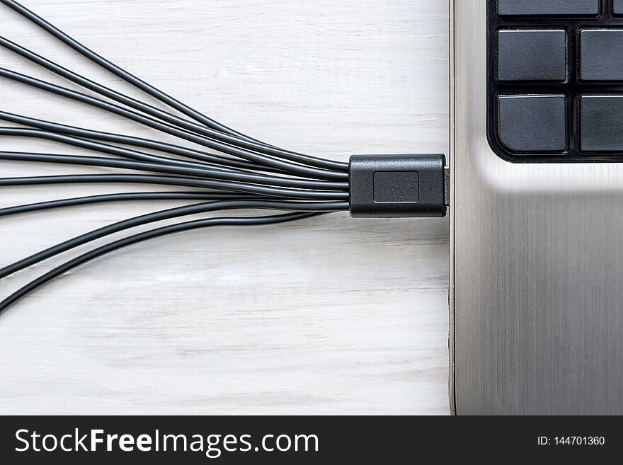 Black USB cables connected to laptop on white wooden background