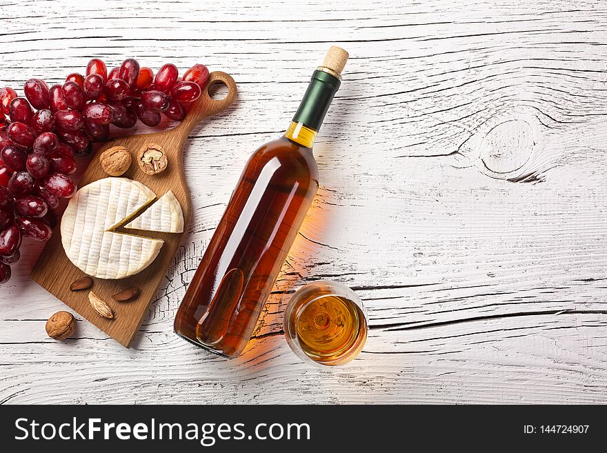 White wine bottle, grape, cheese and wineglass on white wooden board. Top view with copy space