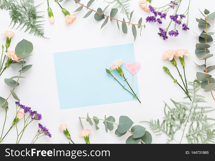 Flowers composition. Paper blank, carnation flowers, eucalyptus branches on pastel  background. Flat lay, top view, copy spaceFlat