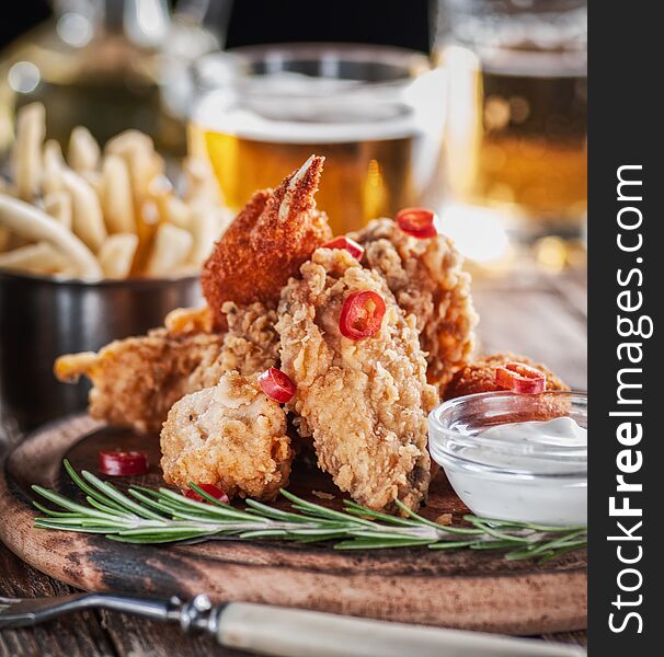 Chicken wings in a batter with beer and fries on a wooden plate with sauce
