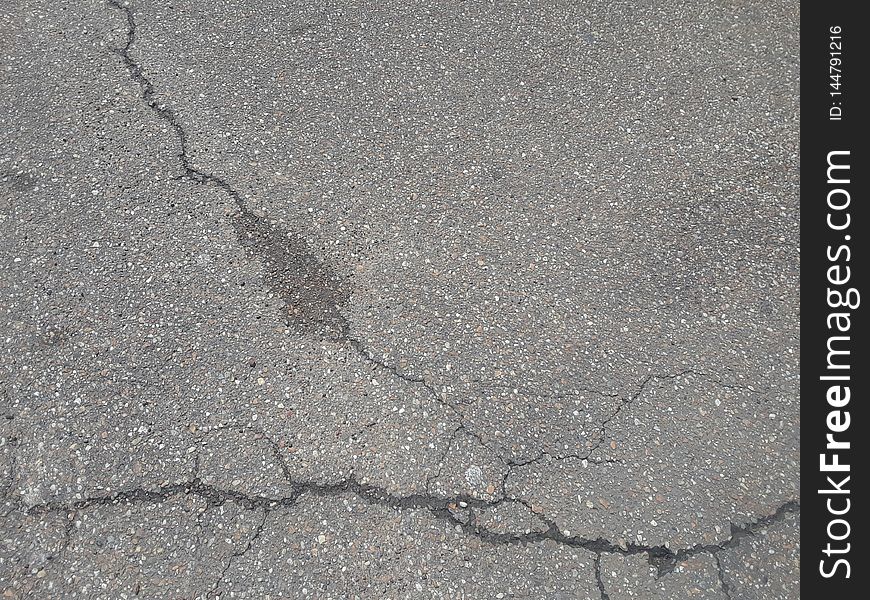 An old, worn asphalt pathway with multiple fractures on the surface. An old, worn asphalt pathway with multiple fractures on the surface.