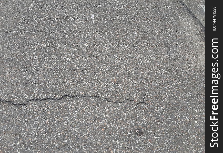 An old, worn asphalt pathway with multiple fractures on the surface. An old, worn asphalt pathway with multiple fractures on the surface.