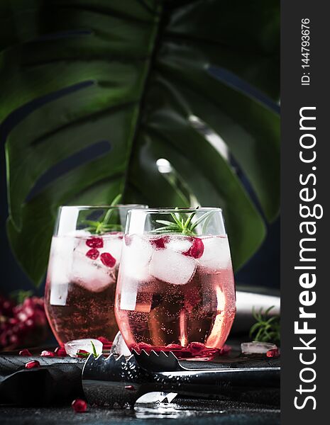 Red cocktail with cold vodka and pomegranate juice, ice cubes and rosemary, bar tools, blue black bar counter background, copy