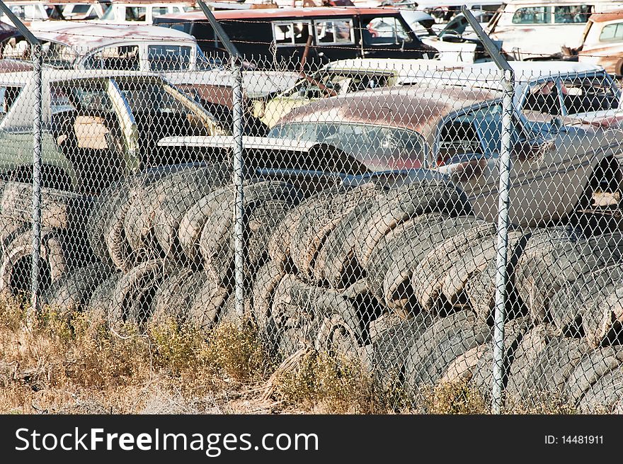 Old vehicles being recycled for parts and scrap metal in an auto salvage yard. used tires in the foreground