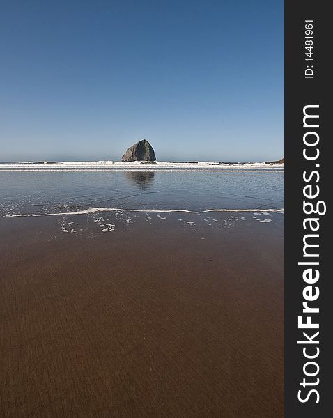 Early morning low tide with sand that looks like it has been groomed and a haystack rock complete with water reflection. Early morning low tide with sand that looks like it has been groomed and a haystack rock complete with water reflection.