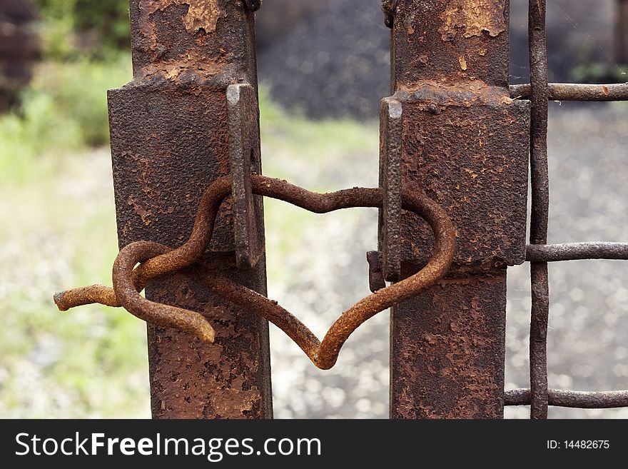 A rusty iron lock in the form of heart hanging on a fence. A rusty iron lock in the form of heart hanging on a fence