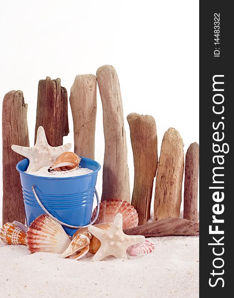 Miniature blue pail filled with sand, starfish and seashell, in front of rustic driftwood fence. Seashells and starfish surrounding base of pail. Miniature blue pail filled with sand, starfish and seashell, in front of rustic driftwood fence. Seashells and starfish surrounding base of pail