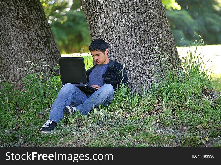 Boy along side of tree with laptop computer. Boy along side of tree with laptop computer