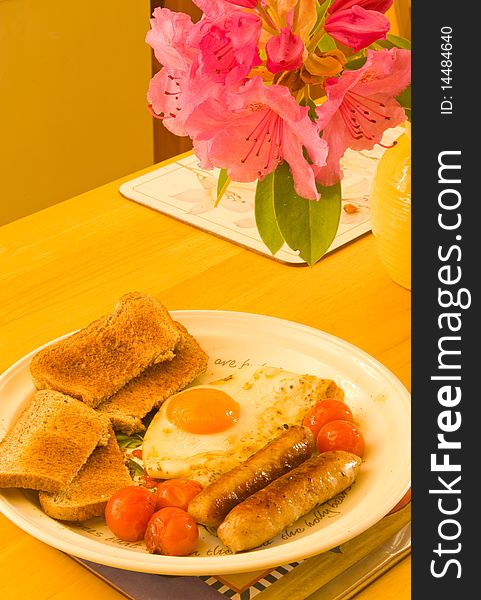An image of sausage, fried egg, cherry tomatoes and toast on a table with a jug of flowers. . An image of sausage, fried egg, cherry tomatoes and toast on a table with a jug of flowers. .