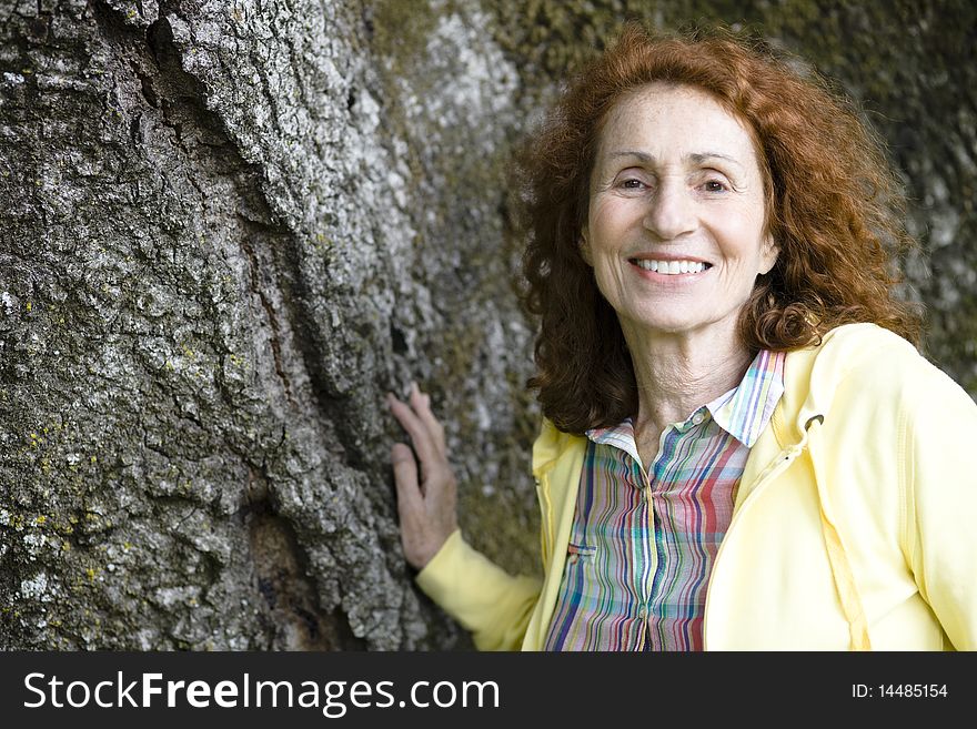 Portrait of a Pretty Senior Woman With Red Hair Touching a Treetrunk. Portrait of a Pretty Senior Woman With Red Hair Touching a Treetrunk