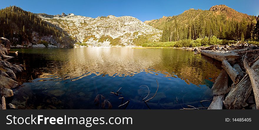 Clear pristine alpine lake flanked by granite peaks and logs. Clear pristine alpine lake flanked by granite peaks and logs.