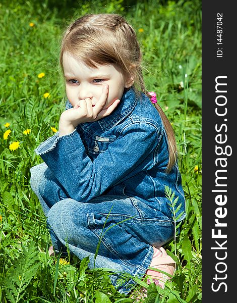 The thoughtful girl sits on a grass and looks in a distance. The thoughtful girl sits on a grass and looks in a distance