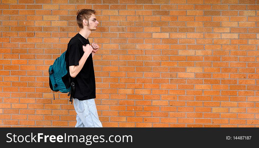 A tall white Caucasian young adult teenage male walks in front of a brick wall. Lots of room for your copyspace text. He has a backpack and glasses. A tall white Caucasian young adult teenage male walks in front of a brick wall. Lots of room for your copyspace text. He has a backpack and glasses