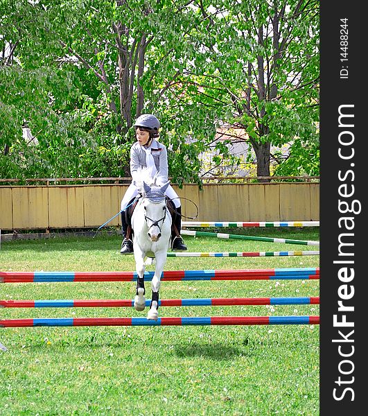 Young children jockey riding beautiful racial white aristocratic England horse in parkour competition. Young children jockey riding beautiful racial white aristocratic England horse in parkour competition