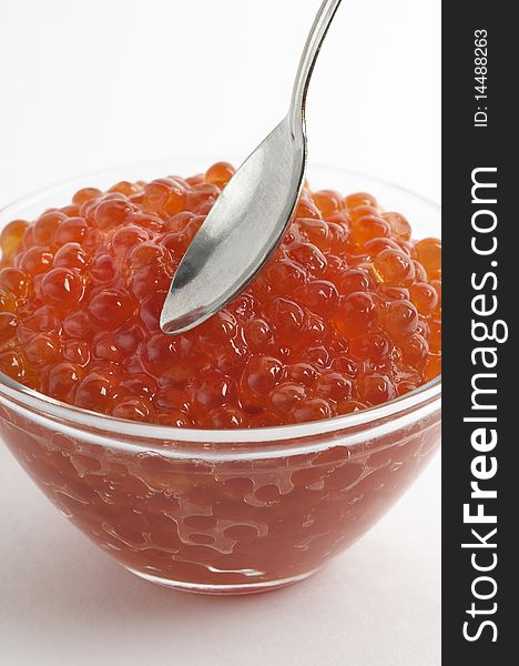 Red caviar in the little glass bow and spoon fragment isolated over white background