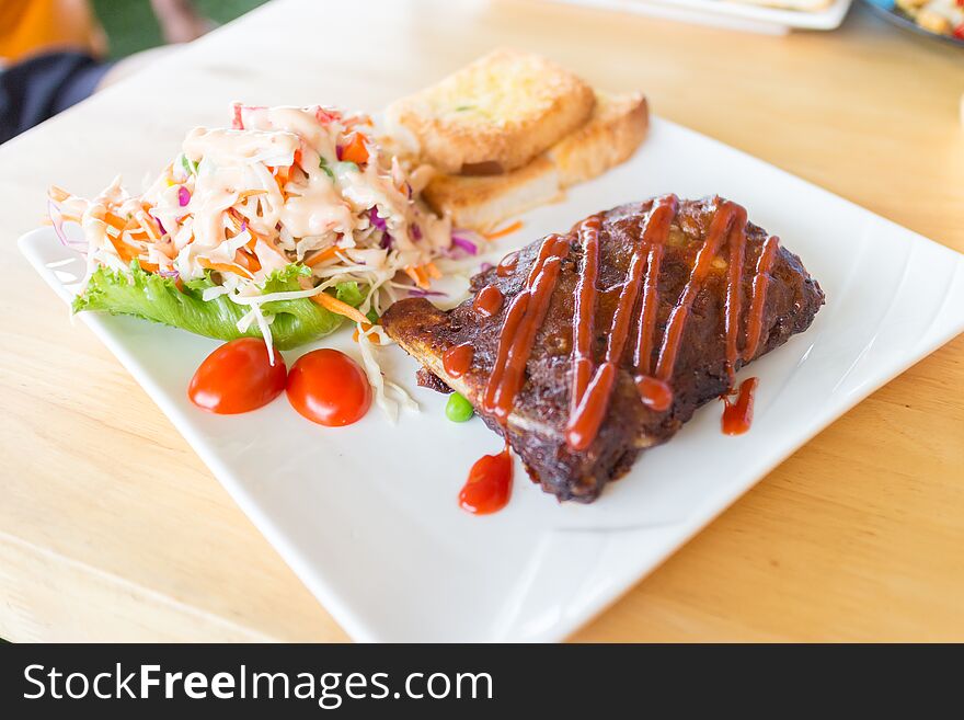 Close up view of pork barbecue ribs with barbecue sauce that served with garlic bread and vegetable salad