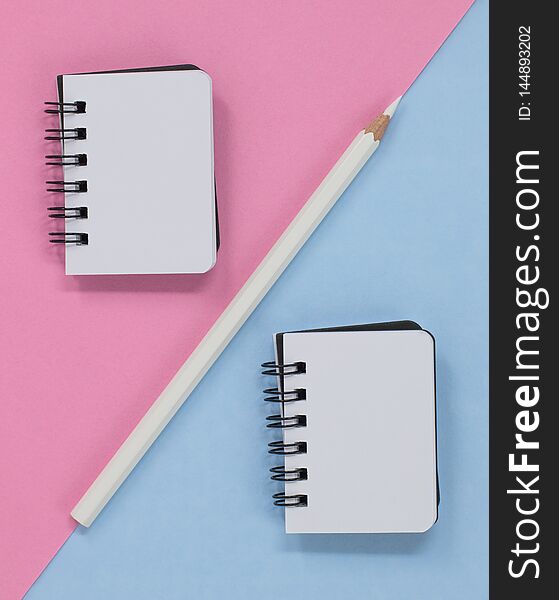 Two open spiral notebooks pencil on a pink and blue diagonal background. Flat lay with copy space