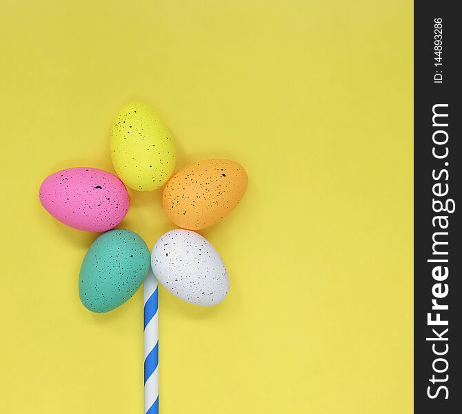 Single flower made from colourful easter eggs against a yellow background, with copy space for text. Single flower made from colourful easter eggs against a yellow background, with copy space for text.