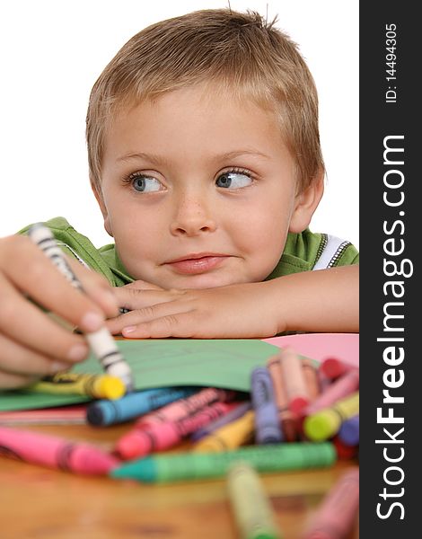 Young blond boy resting his head on his hand, crayons and colorful paper in front of him. Young blond boy resting his head on his hand, crayons and colorful paper in front of him