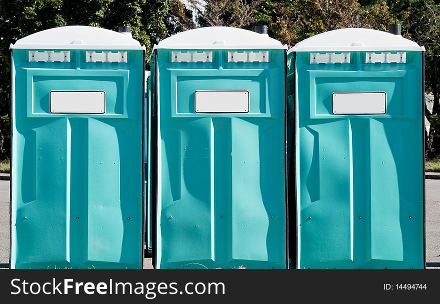Three green portable johns standing in a row outdoors. Three green portable johns standing in a row outdoors