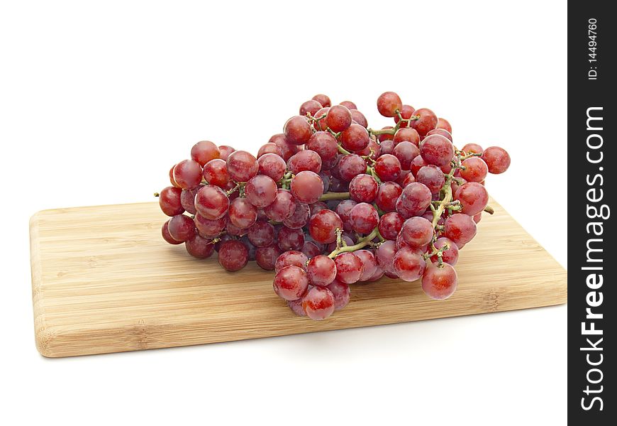 Bunch sweet red grapes on wooden cheeseboard isolated on white. Bunch sweet red grapes on wooden cheeseboard isolated on white