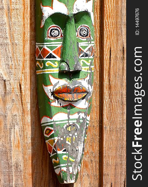 A detailed painted wooden mask hung against wooden paneling. A detailed painted wooden mask hung against wooden paneling.