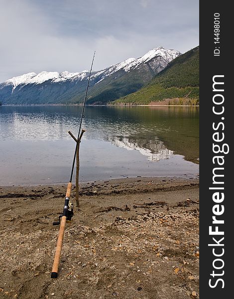 A fishing rod is propped up at a lake shoreline in hopes of catching a fish. A fishing rod is propped up at a lake shoreline in hopes of catching a fish